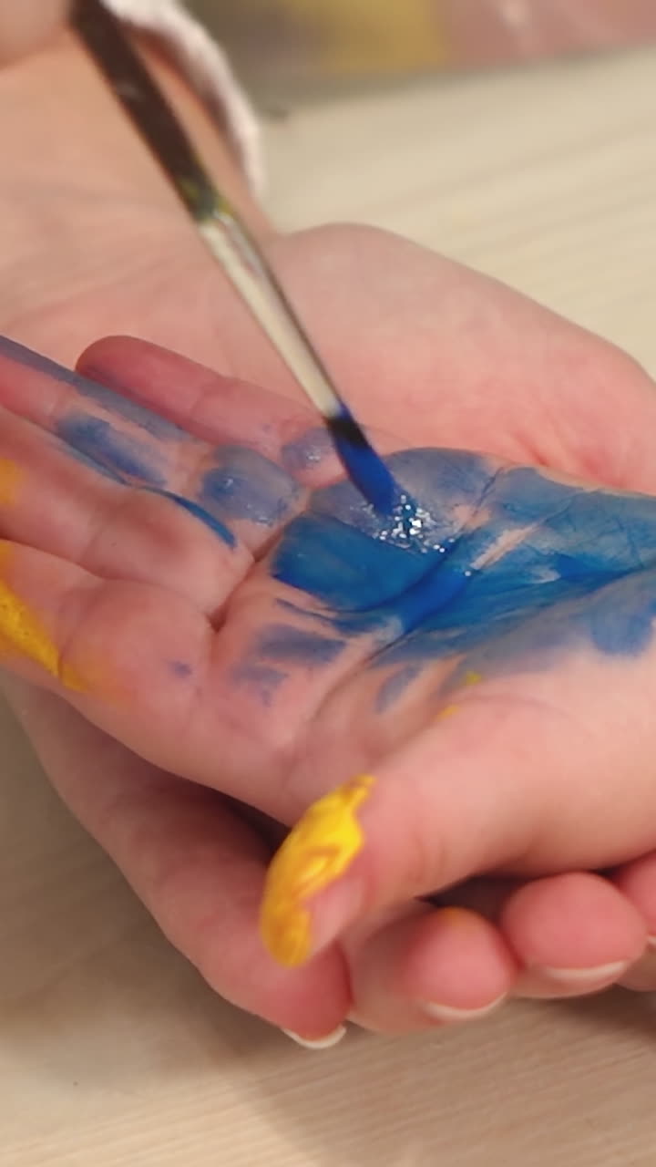 Funny child paints his hands with paint. Baby artist. Artist with dirty palms in paint. Vertical video