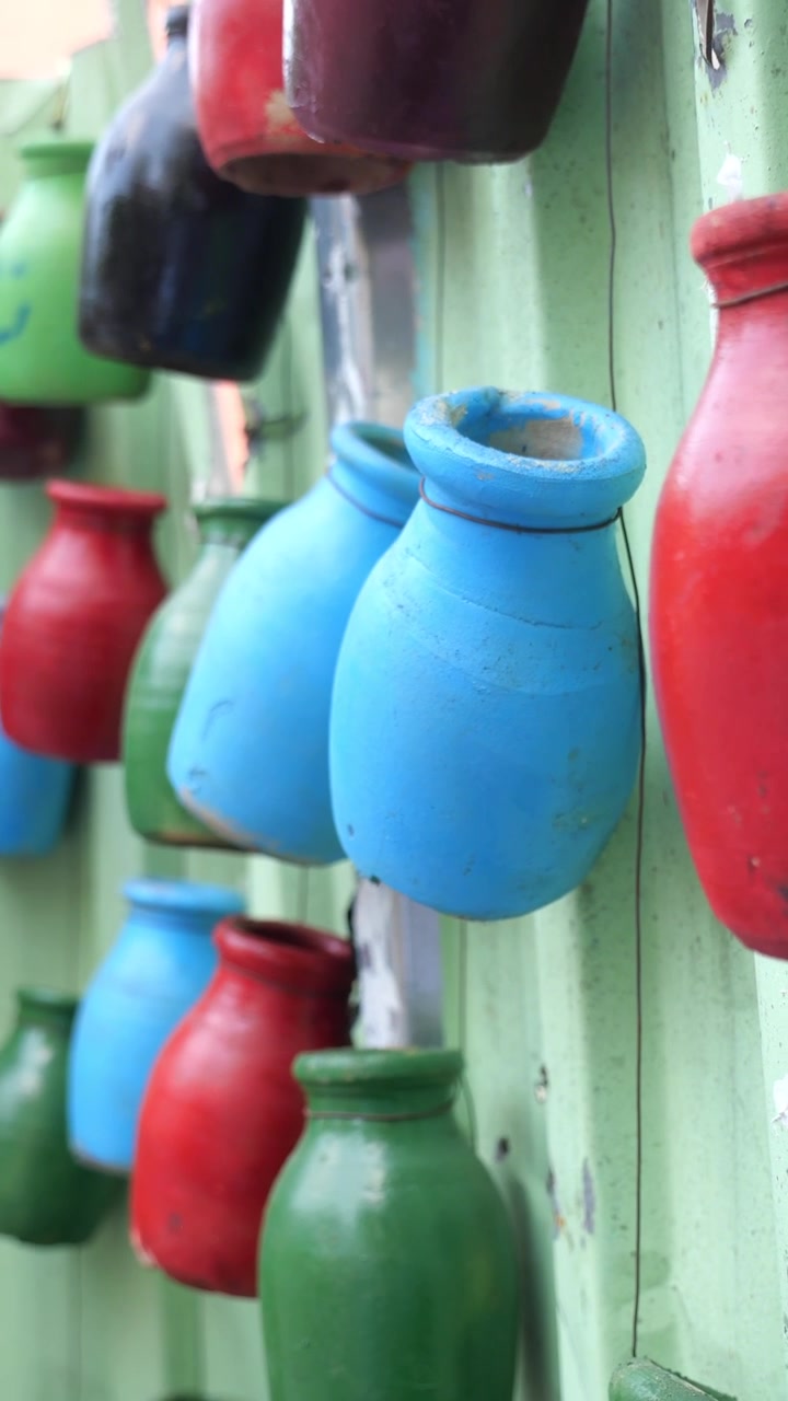 Vasi in terracotta dipinti e colorati appesi a una parete metallica verde