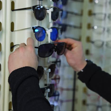 fashionable sunglasses on stand at optics. man testing new glasses in the shop. buyer choosing eyewear in optical store
