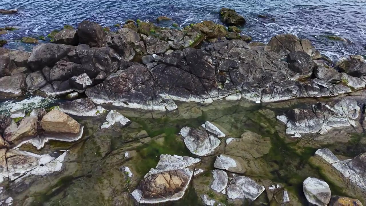 Costa rocciosa con onde che si infrangono durante la bassa marea di giorno in una località costiera