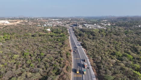 aerial view of a highway winding through a landscape of industry, green hills, and clear skies, showcasing development and nature