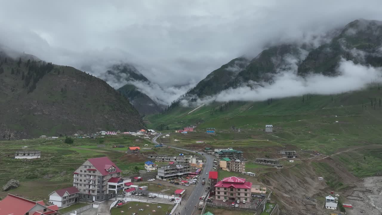 Follow shot of drone over the houses and road between green valley in Naran Batakundi in northern region of Pakistan with low clouds