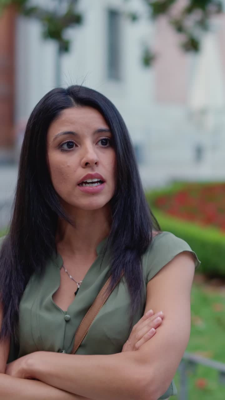 A woman with dark hair in a green shirt speaking and interacting outdoors