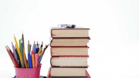 colored pencils in pen holder with pile of books