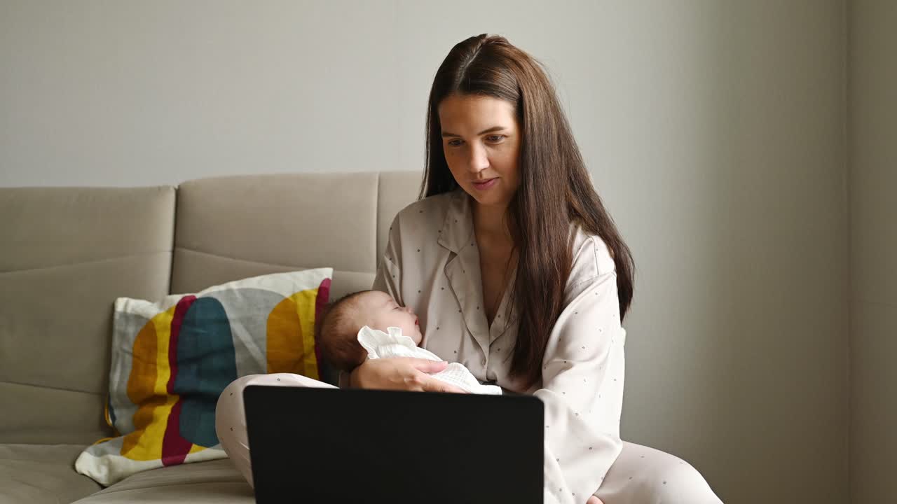 Mother with baby using laptop on sofa