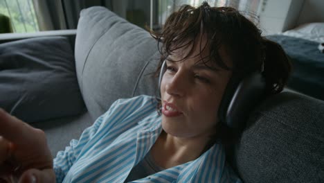 woman relaxing on a couch with headphones and phone