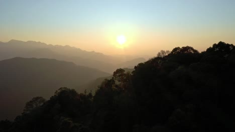 Aerial-forward-shot-showing-silhouette-of-forest-trees-and-mountain-range-during-golden-sunset-in-wilderness