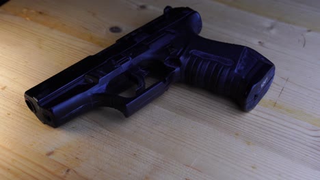 pistola de juguete negra yace plana sobre una mesa de madera y gira con luz amarillenta brillante