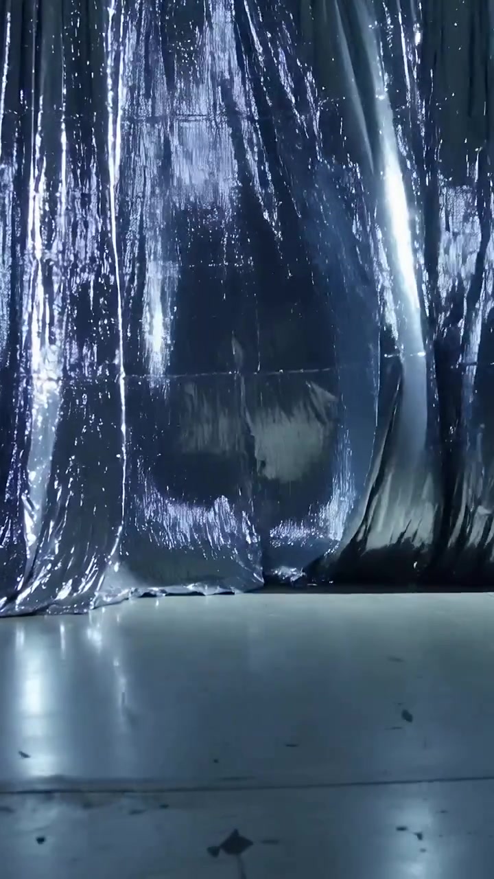 Video verticale: Un impulso luminoso fa sì che una tenda di alluminio formi un rigonfiamento inferiore in studio, rivelando il pavimento.