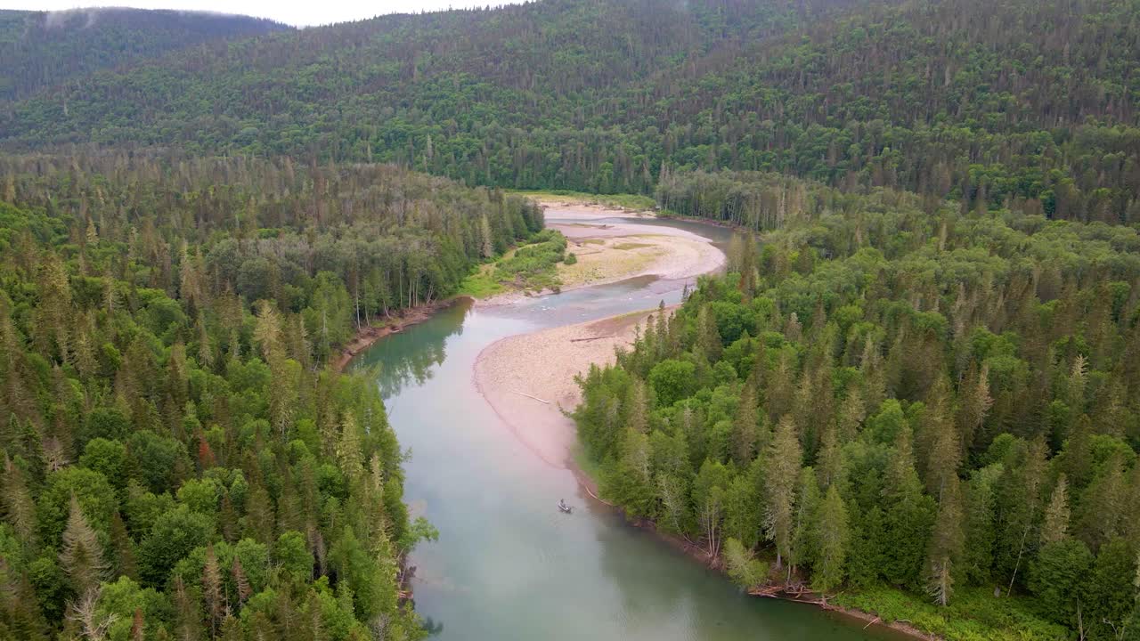 Upea dronemateriaali näyttää turkoosin joen mutkittelevan rehevän vihreän havumetsän läpi, taustalla vuoristoinen maasto.