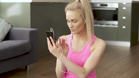 cute woman sitting on yoga mat and browsing mobile phone for songs