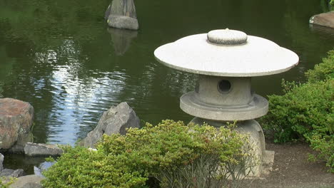 una linterna de nieve japonesa se encuentra en medio de arbustos de azalea al borde del estanque