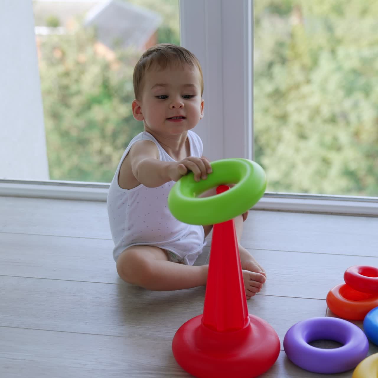 Lovely baby assembling toy pyramid. Caucasian boy plays at home near the window