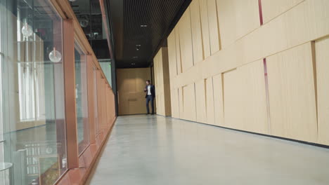 a young businessman with beard in blue suit walks through a hallway carrying a trolley 1