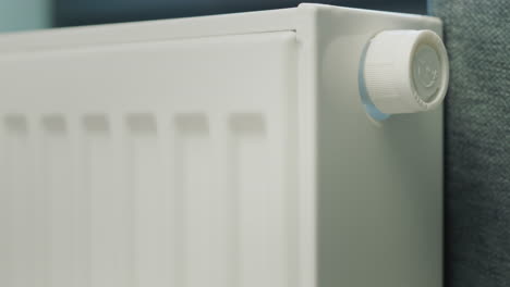 la mano de un hombre regula la temperatura de un radiador de calefacción. conservación de recursos energéticos en una casa particular