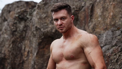 caucasian sportsman with bare chest stands in the rock. athlete flexing muscles to show his athletic build. close up portrait.
