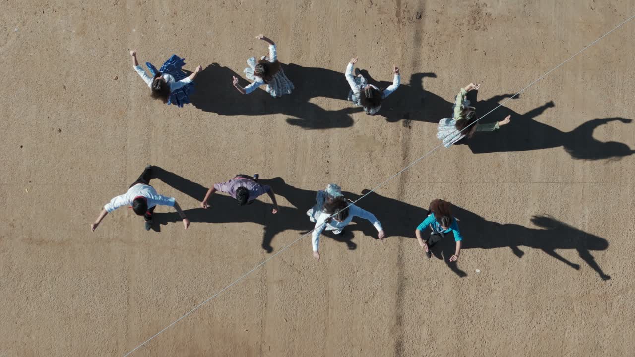 A drone shot overlooking a ceremony in a small South American town of people dancing chacarera. This shot is a zoom-out shot.