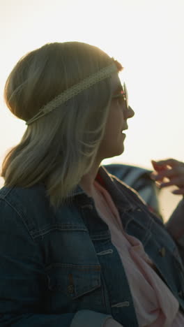a woman adjusts her hair while wearing a headband and denim jacket, with the sun glowing behind her head