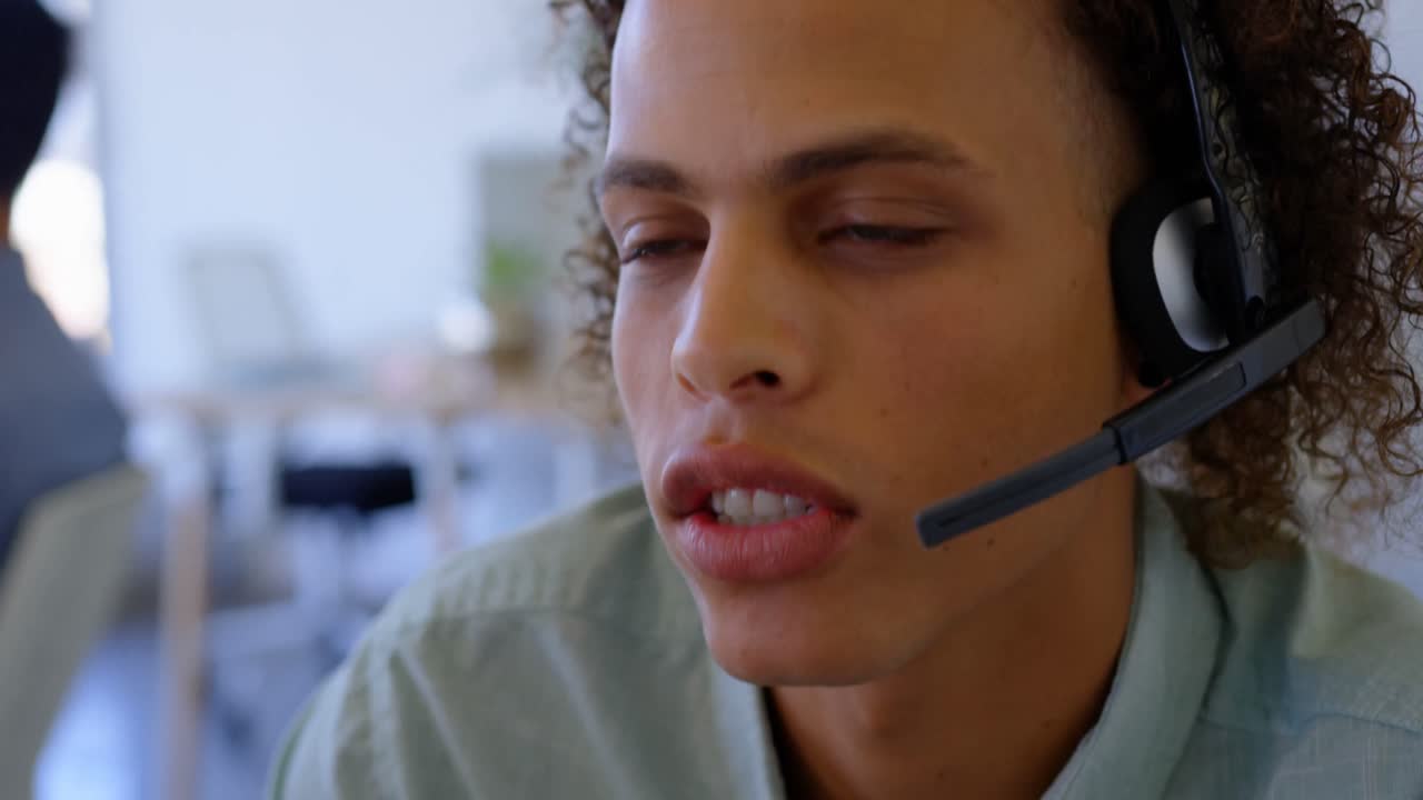 Young mixed-race male executive talking on headset at desk 4k
