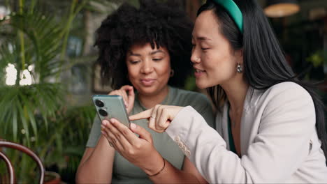 dos amigas mirando un teléfono inteligente en un café