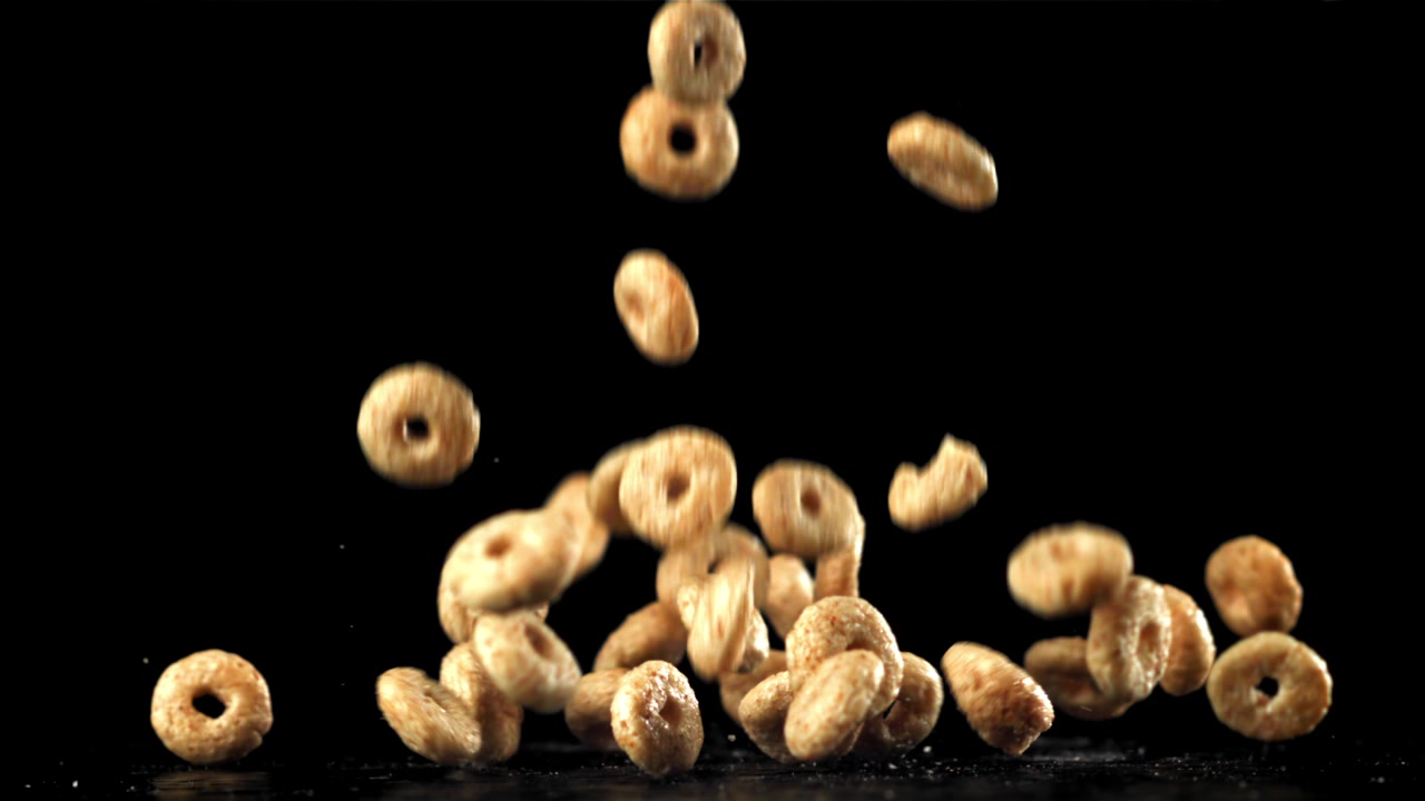 Golden Oat Cereal Rings Falling in Slow Motion on Black Background