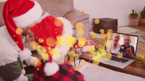 animation of spots over caucasian father and son in santa hats on laptop video call at christmas