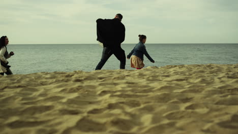 Family-running-sea-beach.-Father-mother-daughter-racing-fun-at-ocean-shore-view.