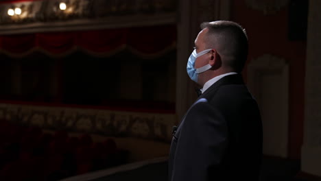theater actor speaks on a stage in medical mask. announcer in suit stands in front of empty theater hall. pandemic concept.