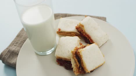 close up of peanut butter and jelly sandwich in a plate with milk on blue surface