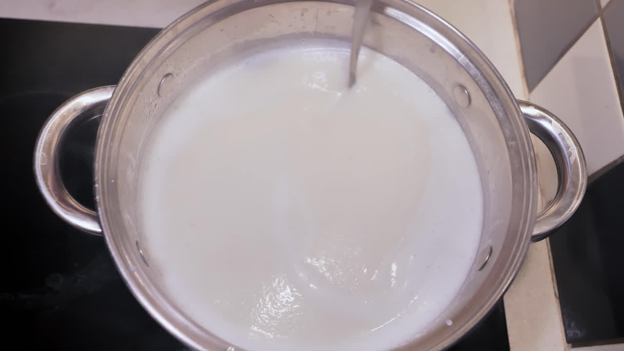 Static overhead of semolina cooking as man stirs gently in warm kitchen light