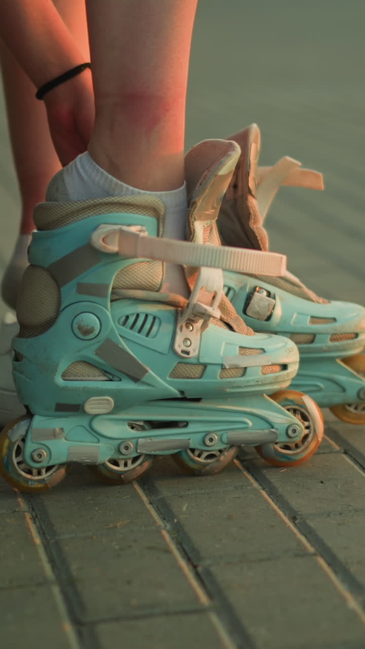 Side view of young lady removing strap of left roller skate while sitting on pavement, with two white sneakers placed next to her, evening lighting creates a calm atmosphere