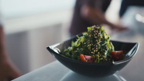 un chef profesional agrega tomates cereza a un plato con algas y semillas, un plato tradicional japonés