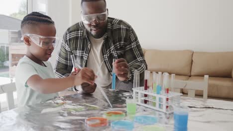 African-american-father-and-son-sitting-at-table-holding-test-tubes-with-liquid,-in-slow-motion