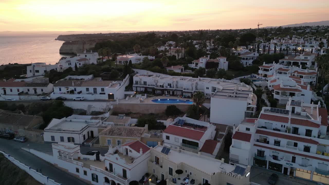 aerial de un dron volando sobre el área de viviendas blancas de carvoeiro algarve, portugal, mientras el dron vuela hacia la puesta de sol en la hora dorada