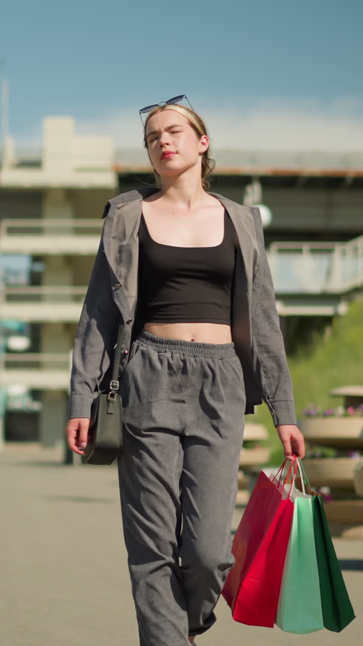 한 여인이 꽃 베스트 근처의 오른손에 쇼핑 가방을 들고 걸어가고, 한 남자가 다리의 레일에 기대어 차가 그녀의 뒤에 있는 오버헤드 다리에서 움직이고 있습니다.