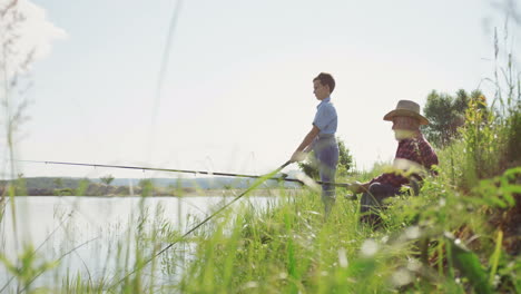 grandfather in a hat fishing with his grandson on a beautiful lake