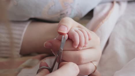 Mother-holding-baby's-hand-while-cutting-fingernail-on-tiny-thumb