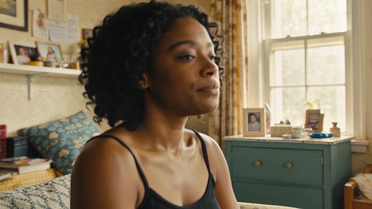 Hearing soft sound, woman in pajamas rising, sitting on bed and turning toward window, teal cabinet