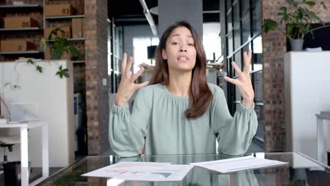 mujer de negocios casual biracial haciendo una videollamada hablando y gesticulando en la oficina, cámara lenta