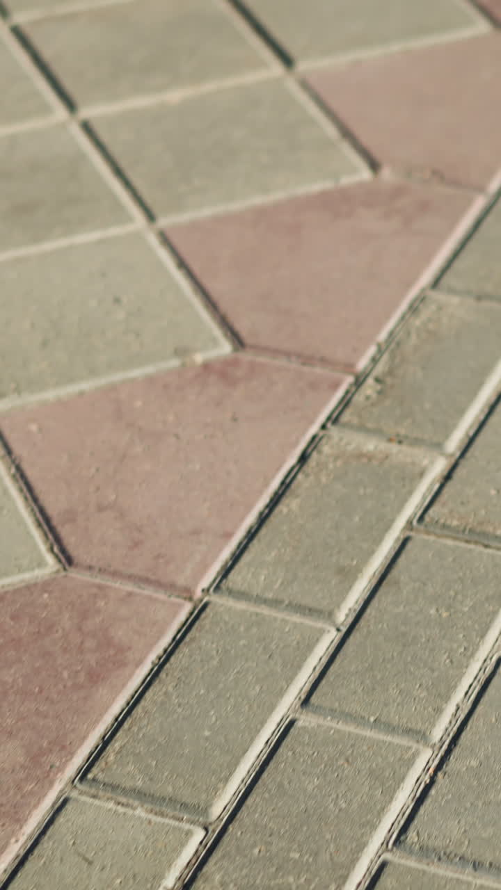 Primer plano de baldosas geométricas en la acera a la luz del sol, diseñador urbano inspeccionando adoquines de hormigón repetitivos con tonos cálidos beige y rosa, poca profundidad de campo y sombras suaves, líneas de lechada visibles