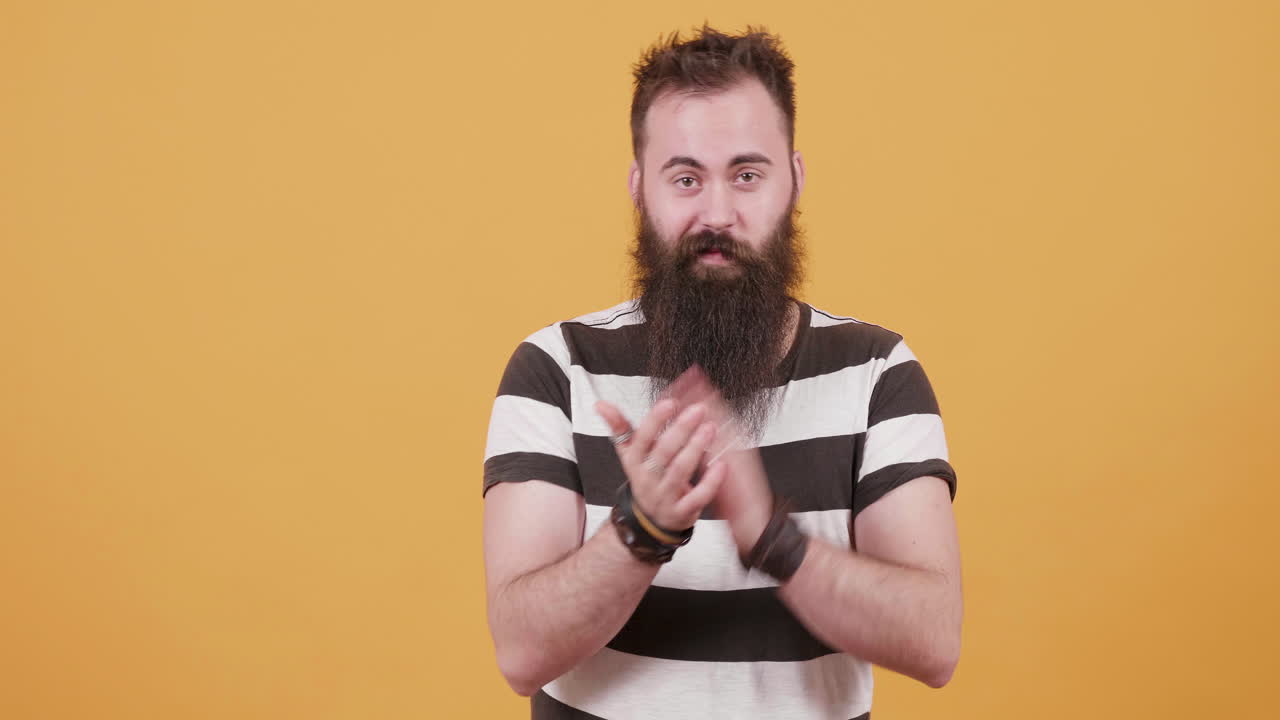 Man with beard clapping in front of an orange background