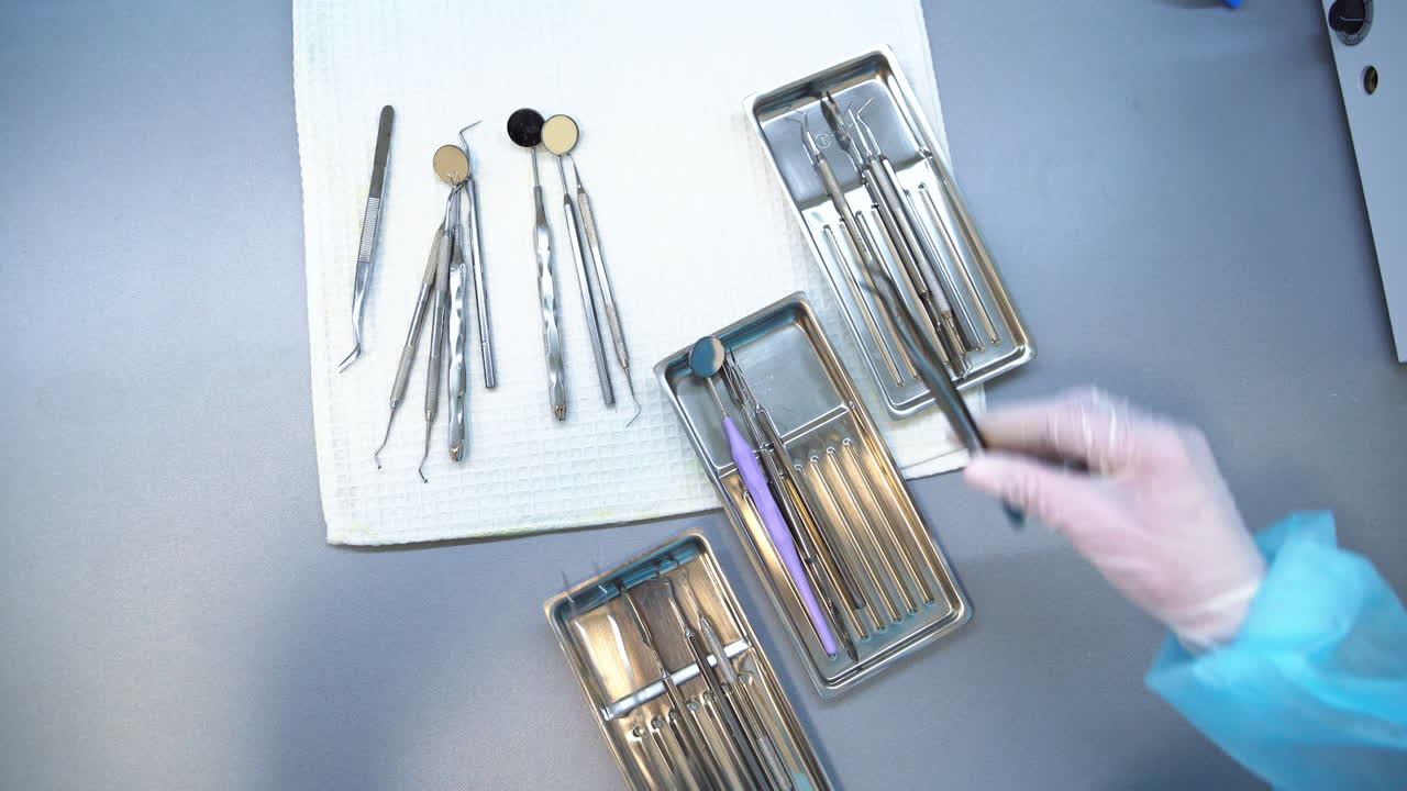 Preparation of metal tools for dental care check up. Nurse's gloved hands take the instruments from a table and divide them into several trays. Close up. Top view.