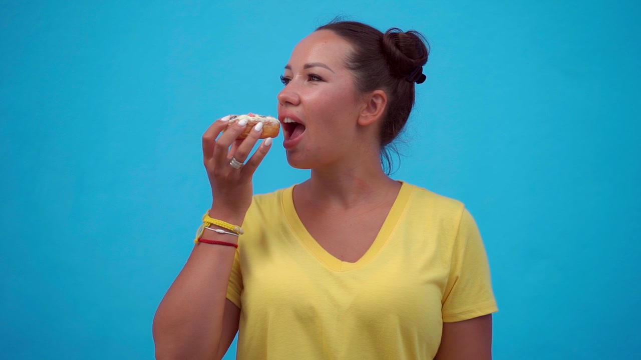 Young Woman Eating a Glazed Donut Against a Blue Background