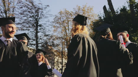 multi ethical joyful friends in traditional graduation gowns and caps hugging and congratulating each other near front of the university building