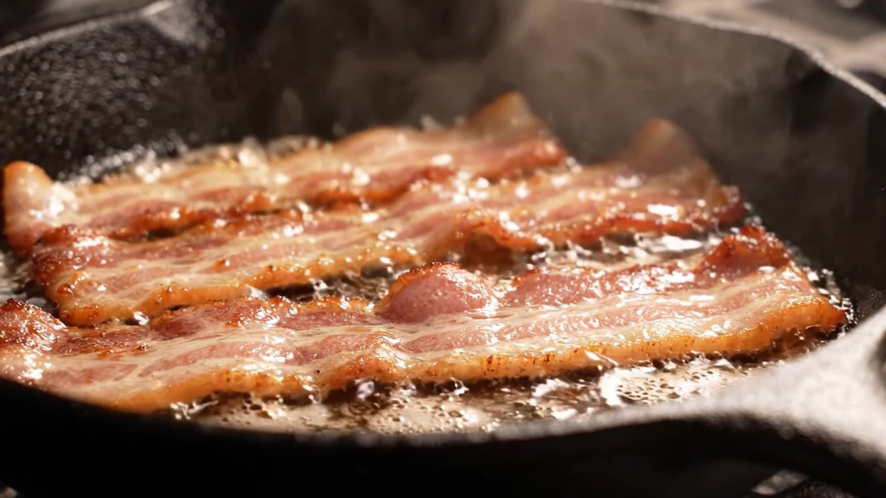 Pancetta sfrigolante che cuoce in una padella di ghisa: Uno spettacolo appetitoso di striscioline croccanti che rilasciano grasso e raggiungono una perfetta consistenza dorata