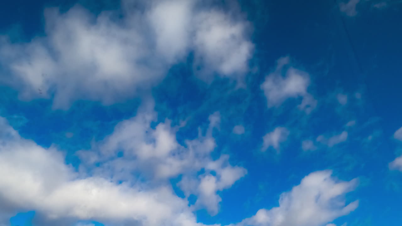 Blue summer sky with little soft white clouds floating quickly. Low angle view. Timelapse.