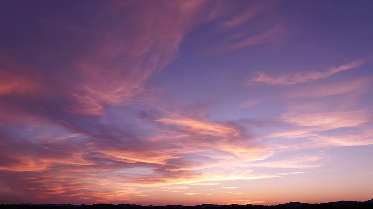 Vibrant sunset sky with colorful wispy clouds over mountains