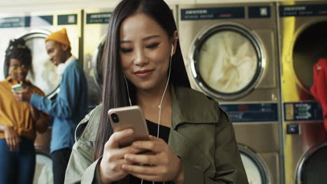 pretty cheerful woman in headphones watching video on smarphone in laundry service room