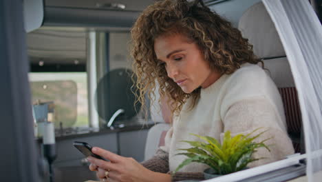 resting freelancer surfing cellphone internet in trailer close up. curly woman