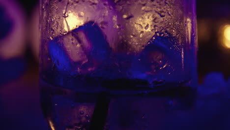 close-up of ice blocks falling into a sparkling drink, alcoholic or non-alcoholic, surrounded by warm lights and night atmosphere